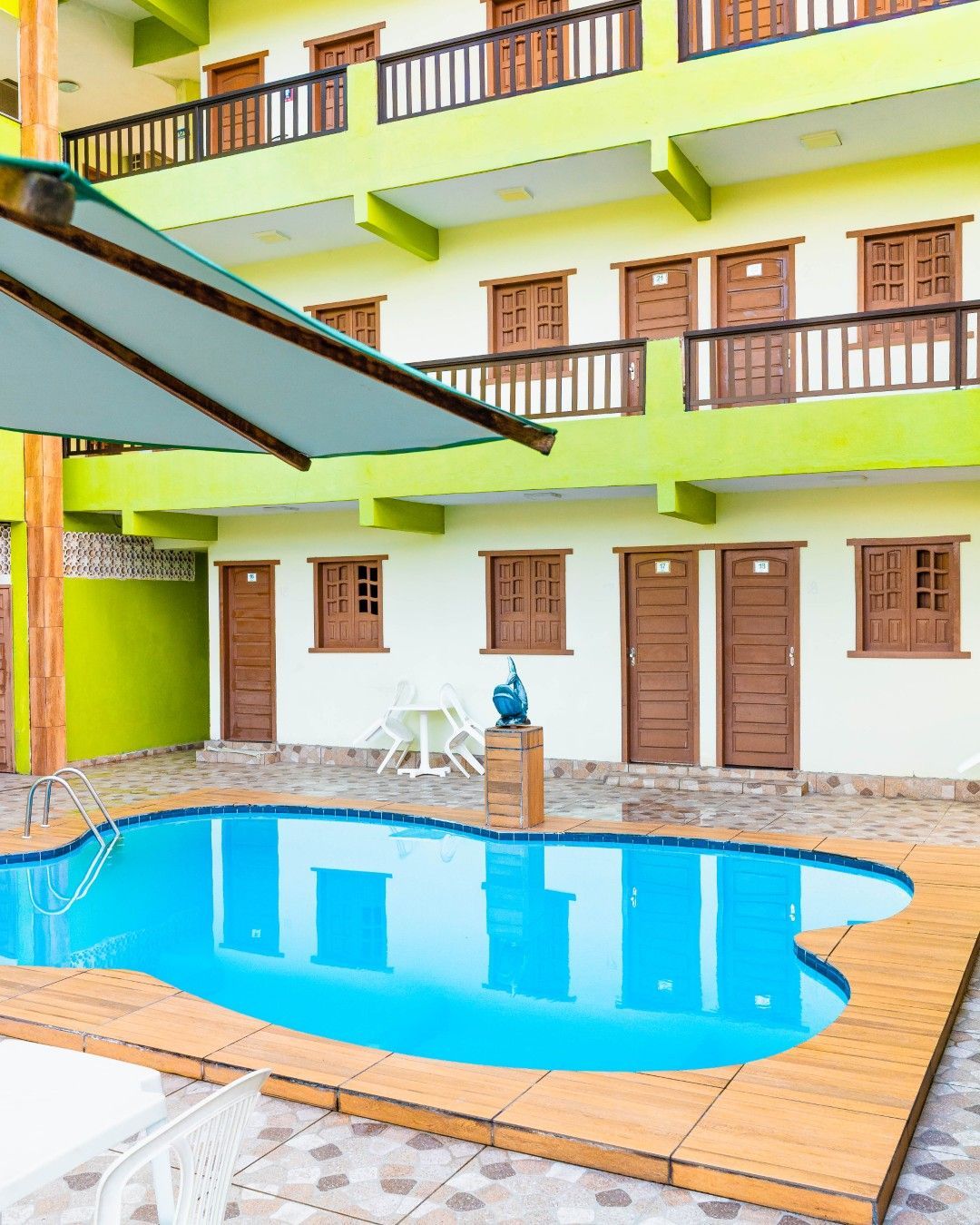 Piscina em frente a um hotel verde-limão e branco com portas marrons e varandas de madeira.