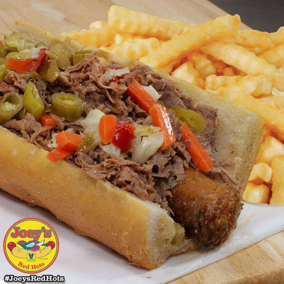 Hot dog with shredded meat and peppers, fries, on a wooden surface.