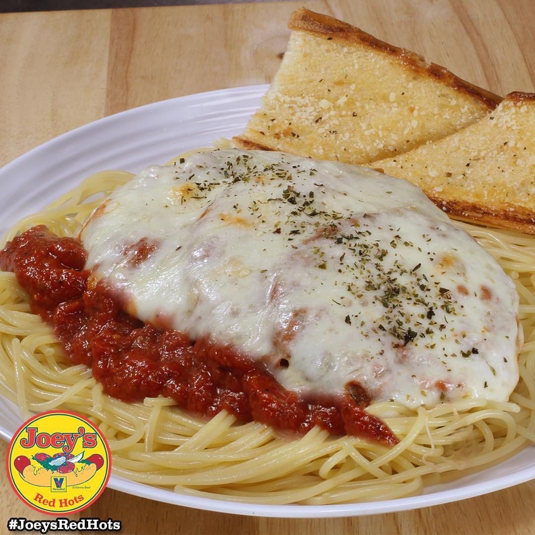 Spaghetti with tomato sauce, topped with melted cheese, served with garlic bread on a white plate.