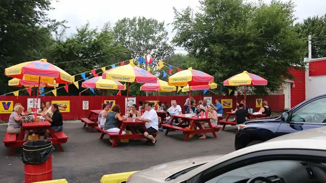 Outdoor seating area with red picnic tables, yellow and red umbrellas, and people eating and socializing.