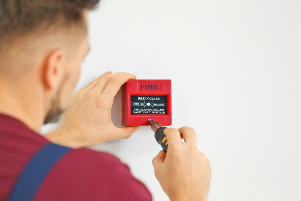 A Man is Installing a Fire Alarm on a Wall — AES Electrical Contracting In Winnellie, NT