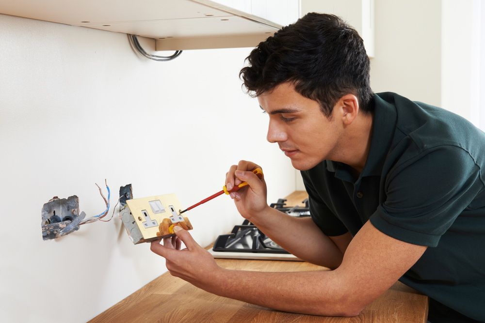 A Man is Working on an Electrical Outlet in a Kitchen — AES Electrical Contracting In Winnellie, NT