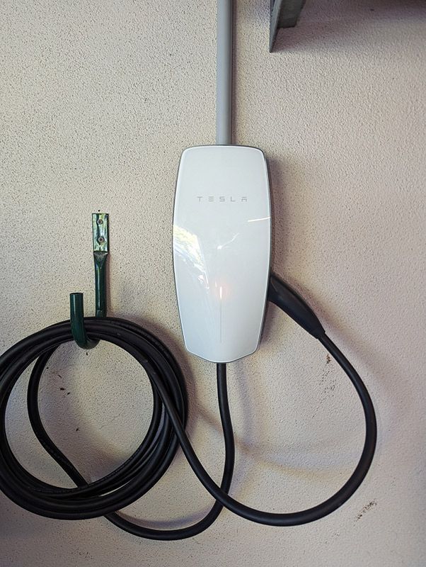 A White Tesla Charger is Hanging on a Wall Next to a Black Cable — AES Electrical Contracting In Winnellie, NT