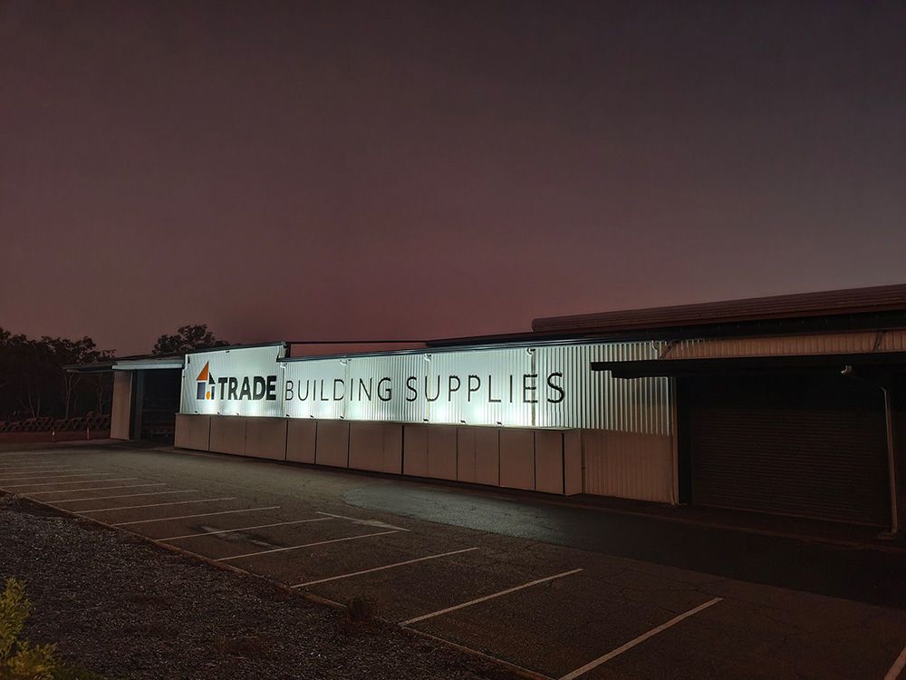 A Building With a Sign That Says Trade Building Supplies is Lit Up at Night — AES Electrical Contracting In Winnellie, NT