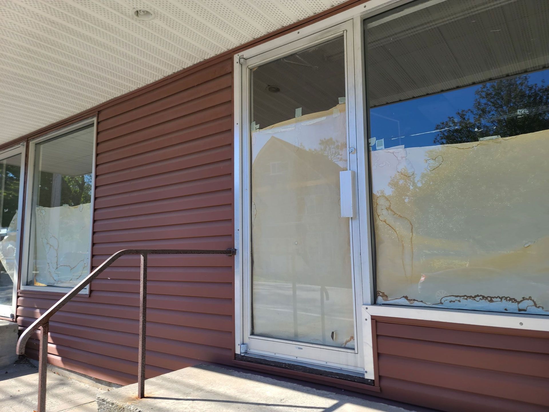Storefront entrance with white door, brown siding, and a metal handrail on the steps