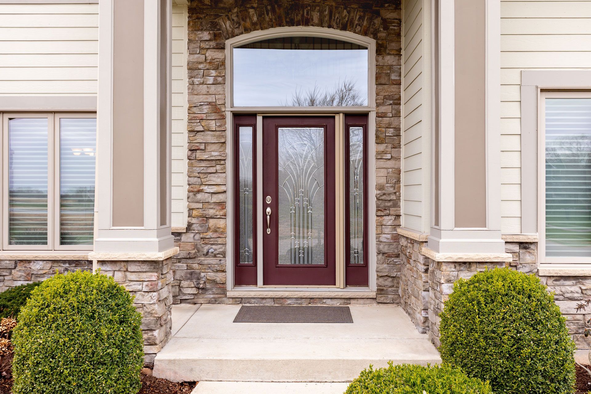 Front entry of a house with a red double door, stone facade, and trimmed bushes