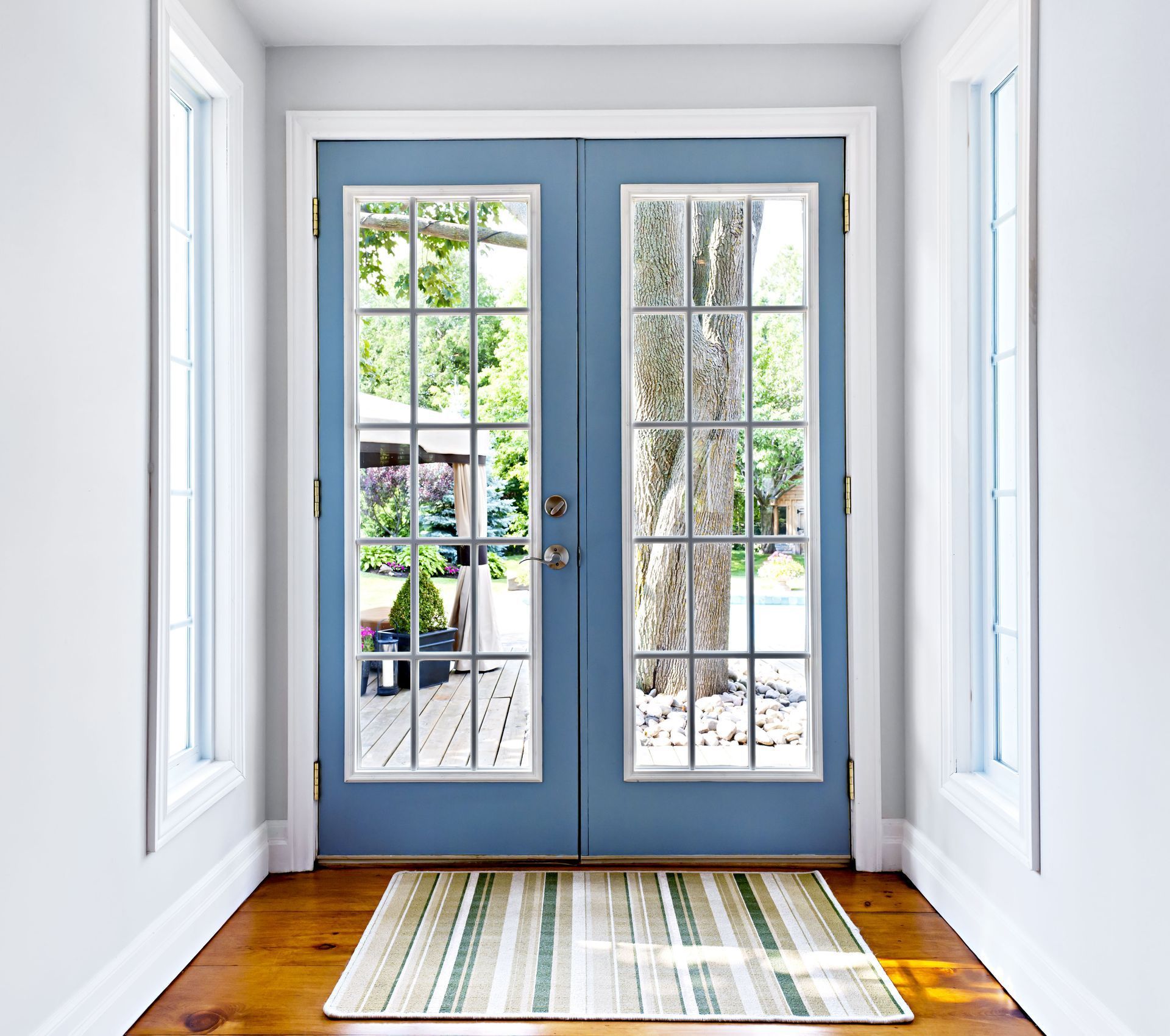 Bright entryway with blue French doors, sidelights, and a striped rug on a hardwood floor.