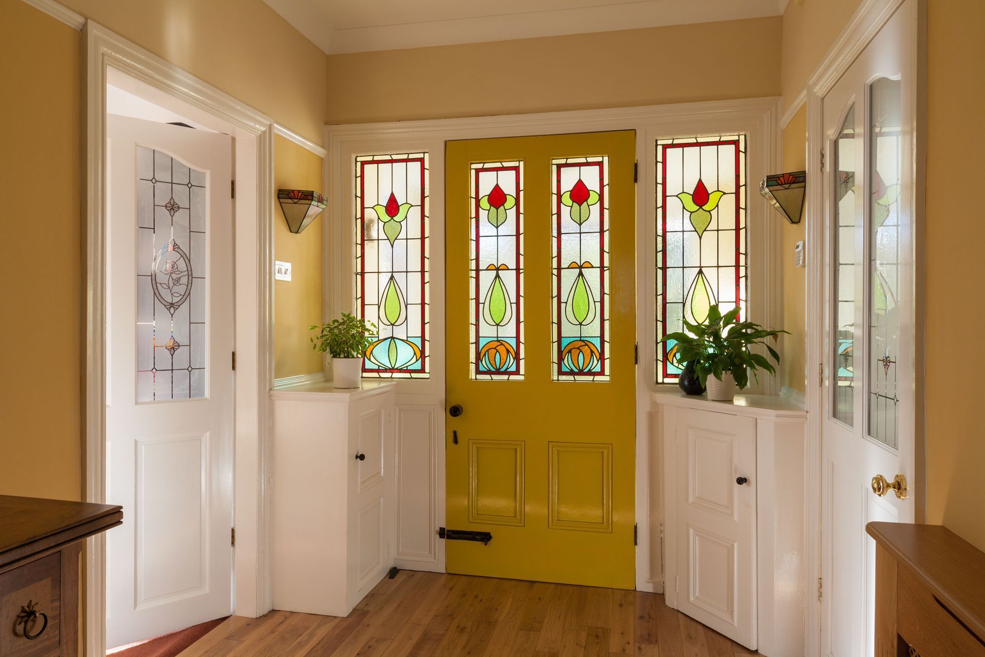 Bright entryway with yellow stained-glass front door, white cabinets, and wood floor