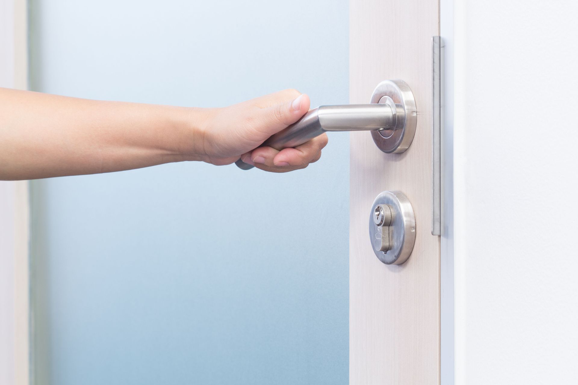 Hand opening a silver door handle on a white door with a lock