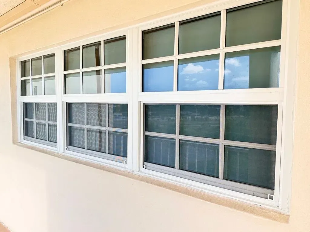 White-framed windows reflecting blue sky on a beige exterior wall
