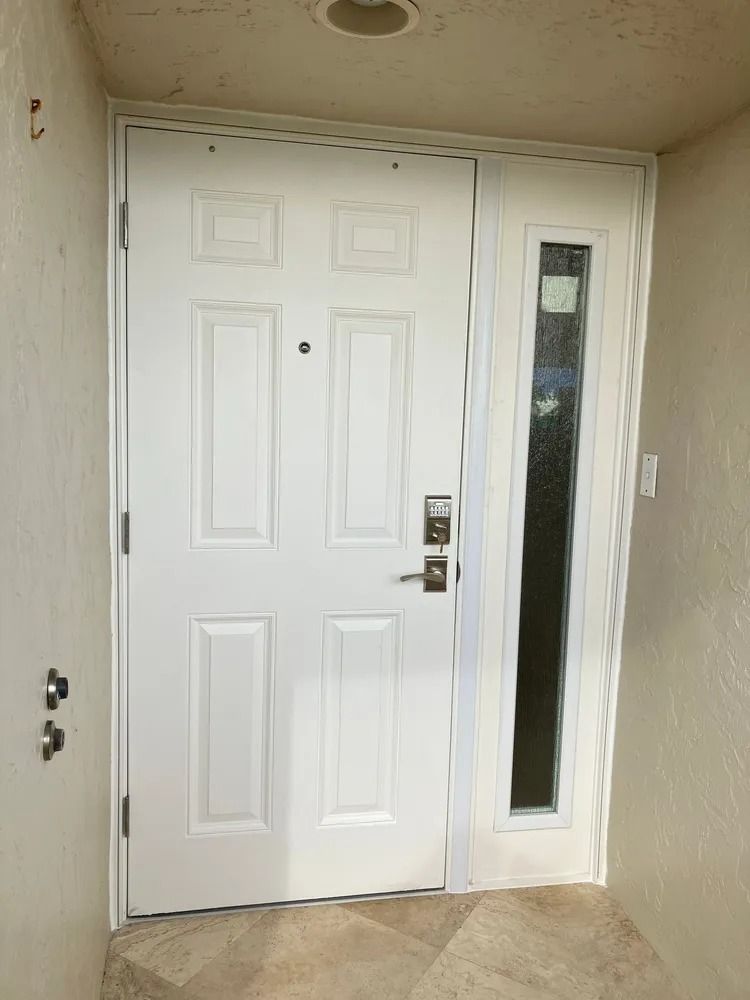 Front door with narrow sidelight window, white trim, and beige exterior wall.