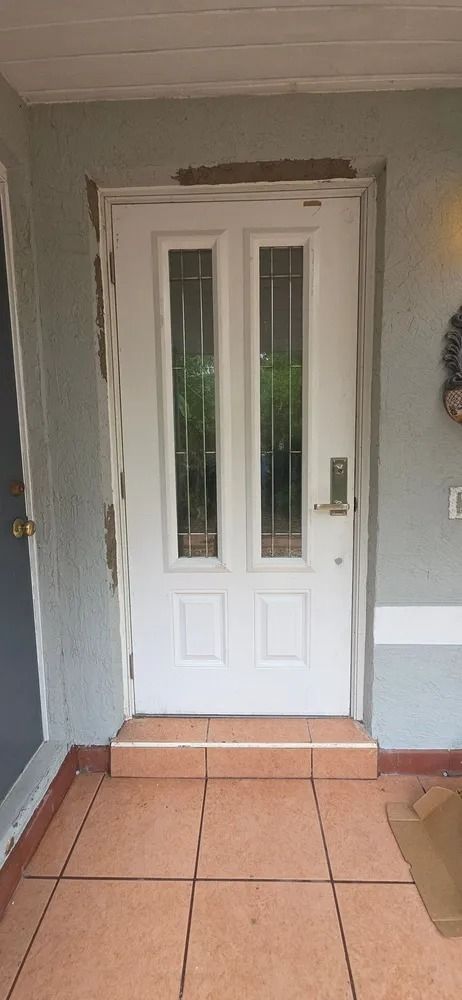 White front door with narrow glass panels in a light green entryway with terracotta tile floor.