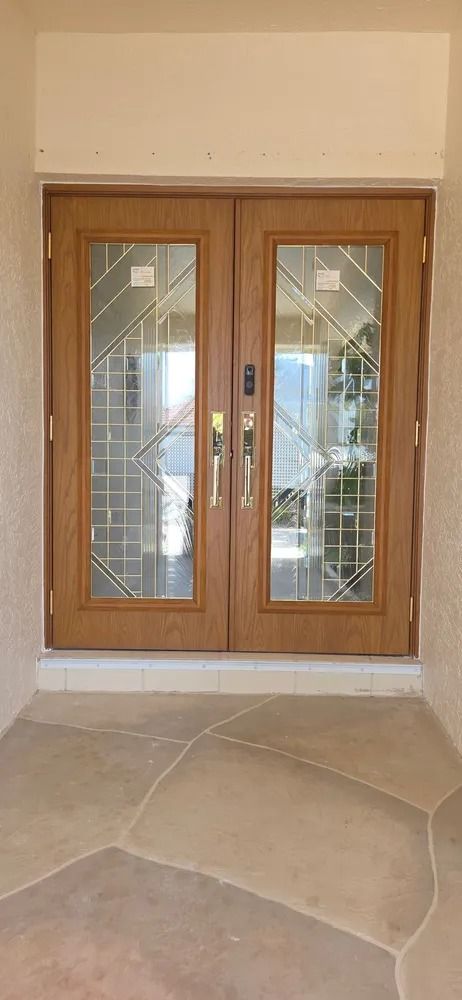 Wooden double front doors with glass panels in a beige entryway, viewed from outside