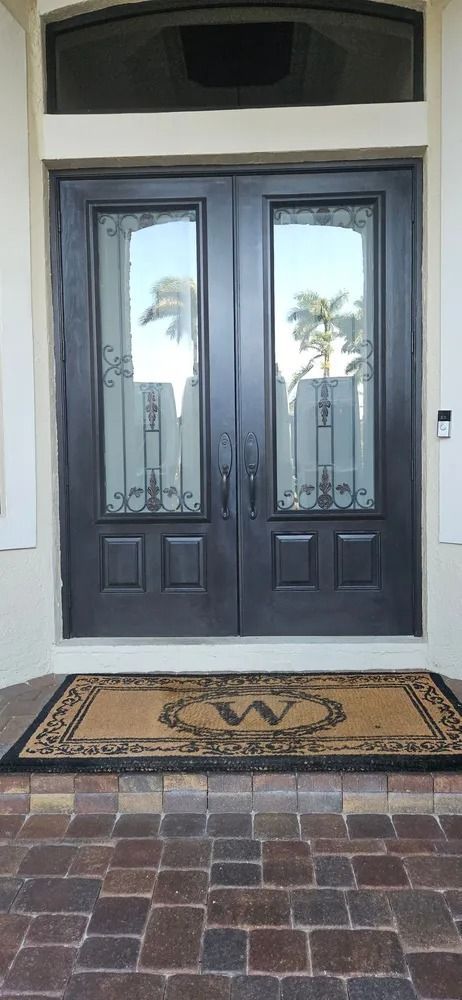 Double front doors with glass panes at a house entrance, above a patterned doormat and brick walkway