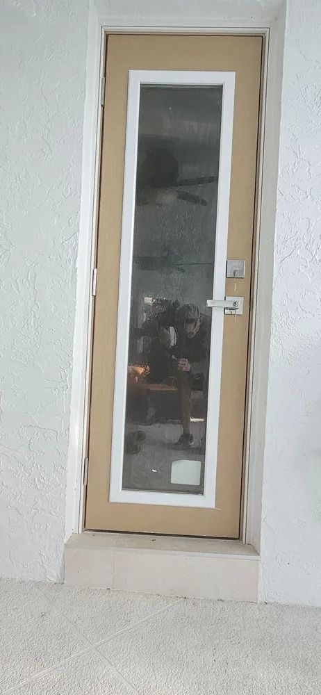 White exterior door with a narrow frosted glass panel and silver handle in a stucco wall.
