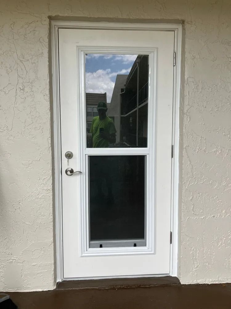 White exterior door with a glass panel and silver handle on a stucco wall