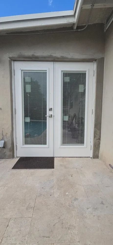 White double glass doors with side panels at a concrete patio entrance under a roof overhang