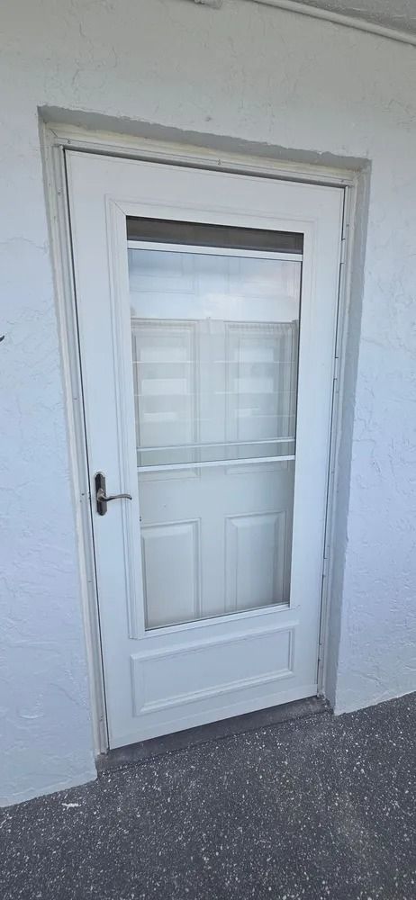 White exterior door with glass panes and a silver handle in a plain wall, above dark flooring