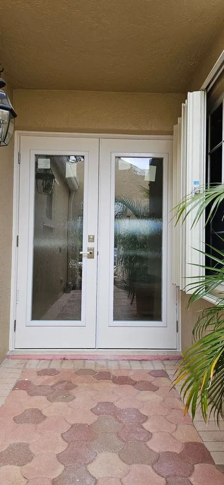 White double front doors at a covered entryway with pink patterned tile flooring.