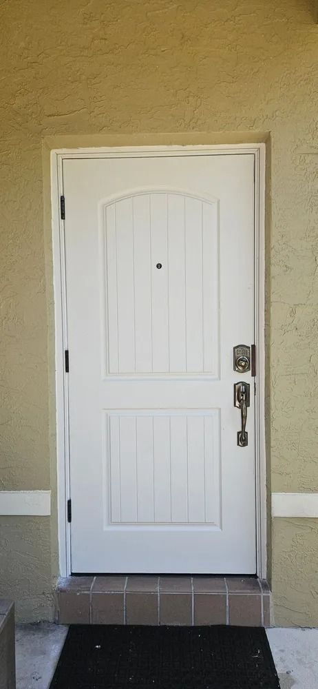 White front door with a silver handle set in a beige wall above a small tiled step
