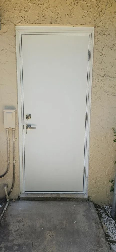 White exterior door with silver handle set in a beige stucco wall above a concrete step.