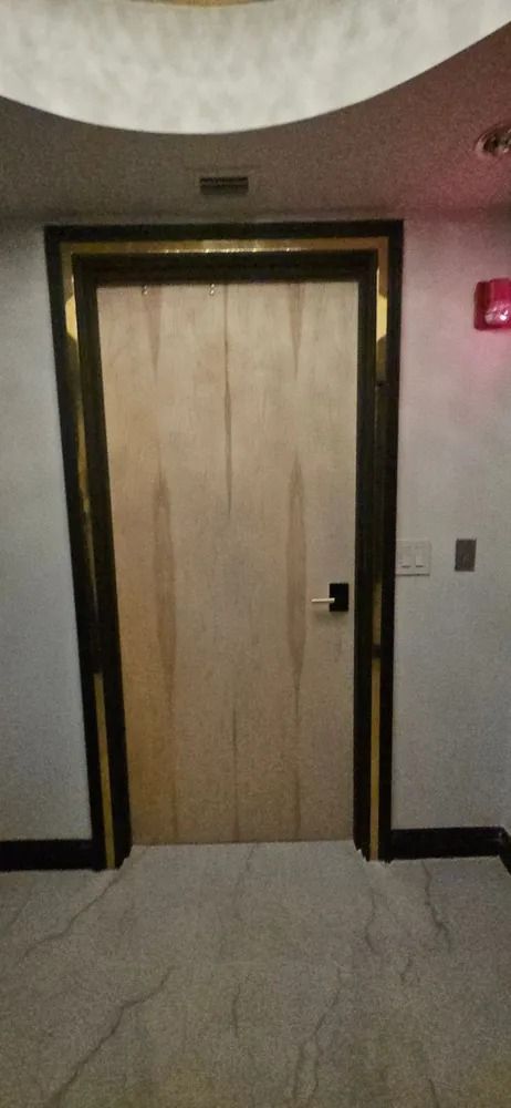 Wooden elevator or room door in a hallway with beige walls and tiled floor.