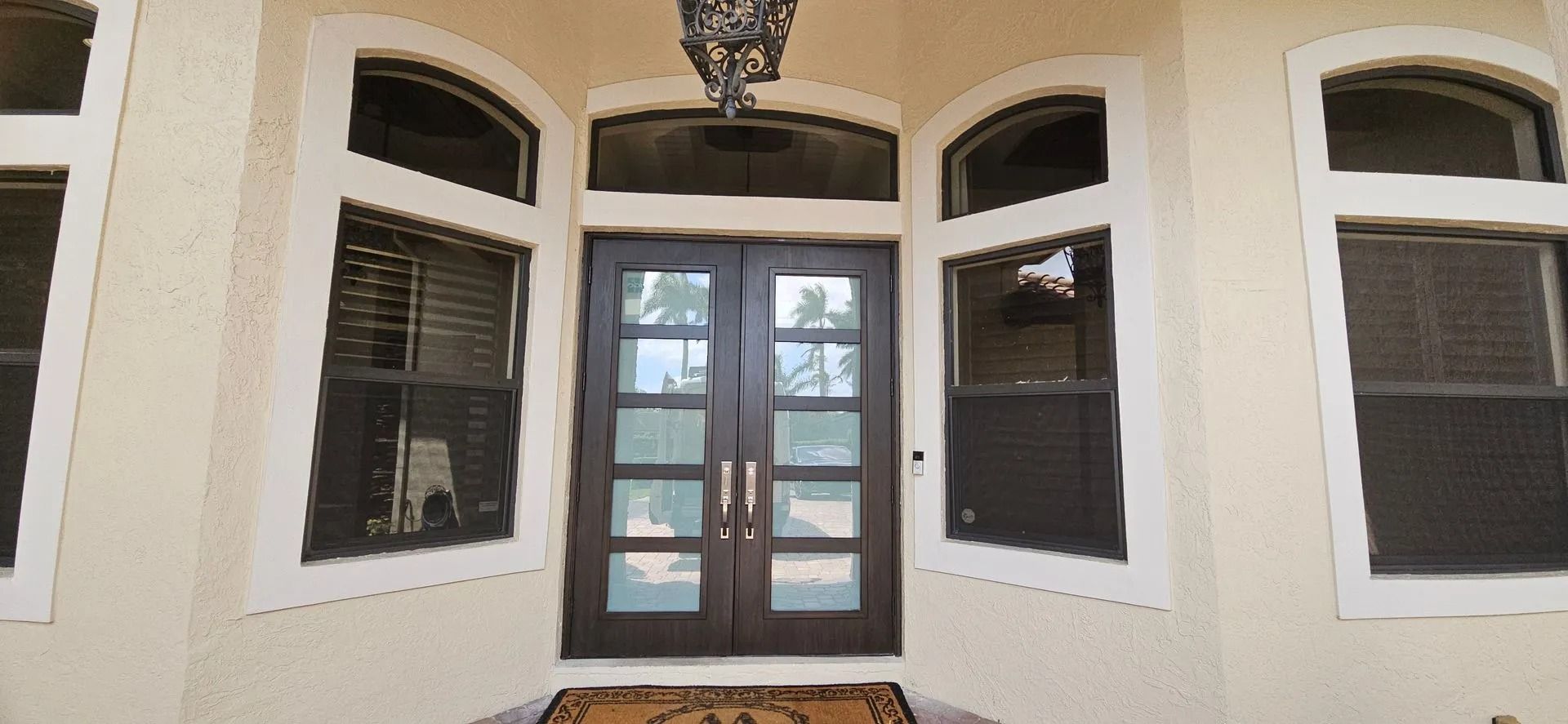 Front entrance with arched windows, double glass doors, and beige stucco walls