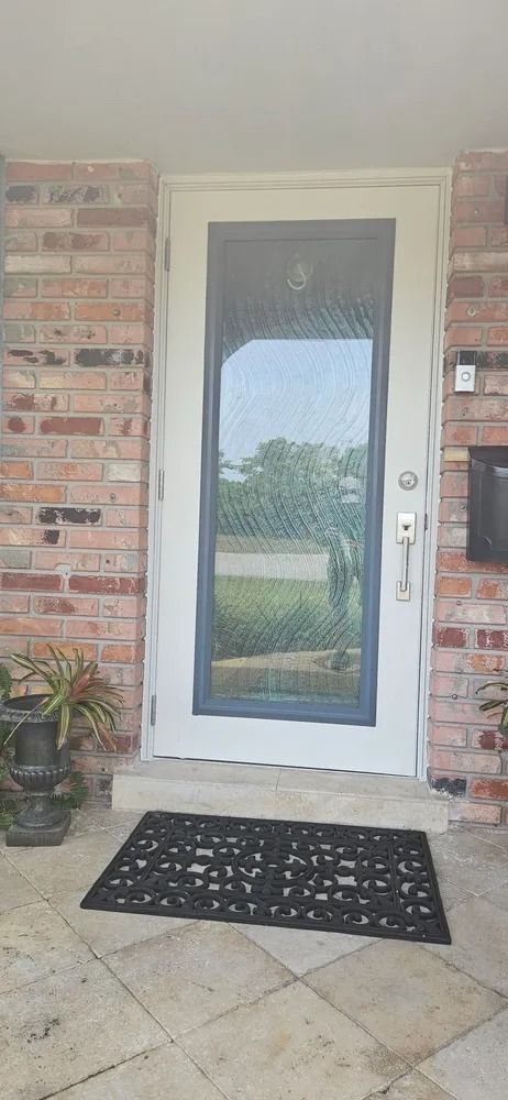 Front porch with a white-framed glass door, brick walls, patterned doormat, and potted plant.