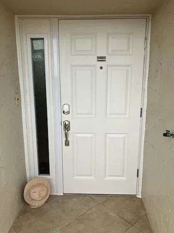 White front door with narrow sidelight in beige entryway; round beige floor mat leaning beside it