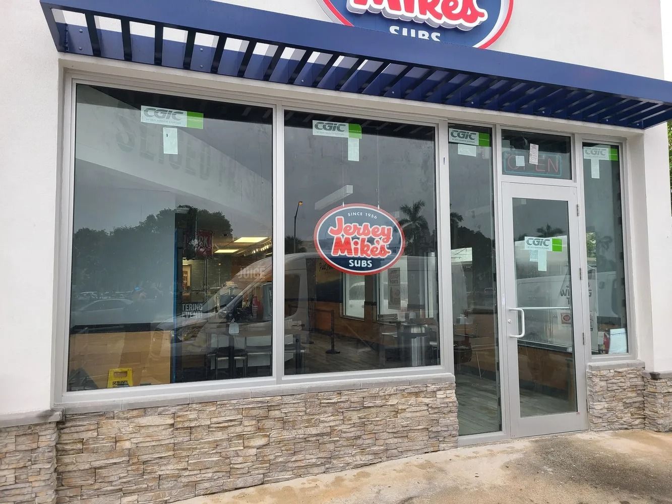 Storefront with large windows, glass door, and stone base under a blue awning.