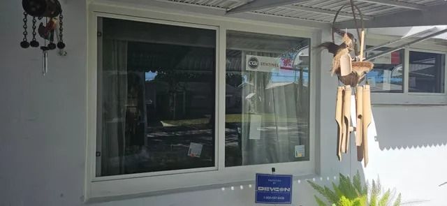 Front porch with a large window, hanging wooden wind chime, and small blue sign on the wall.