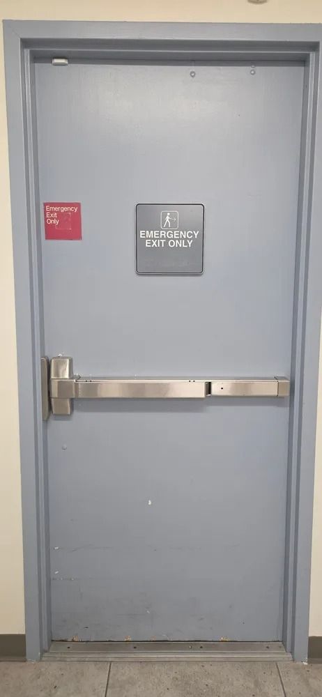 Gray exit door with push bar and EXIT sign, likely a stairwell or emergency exit.