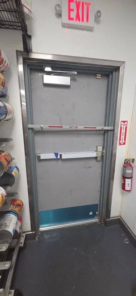 Grey exit door with crash bars and a wall-mounted fire extinguisher in a hallway
