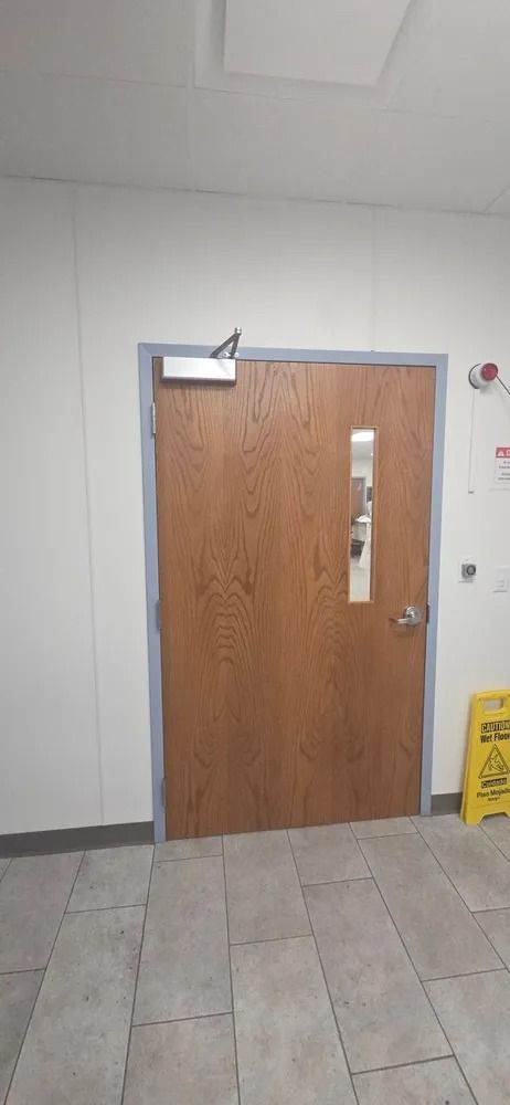 Wooden door with silver hardware in a tiled hallway, with a yellow caution sign nearby