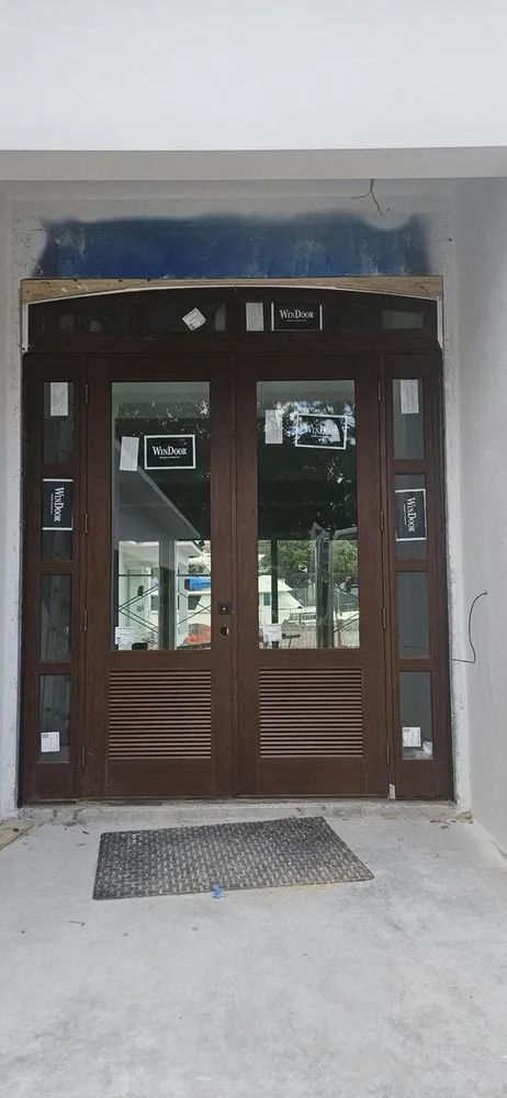 Brown double doors with glass panels at a building entrance, with a doormat and blue awning above.