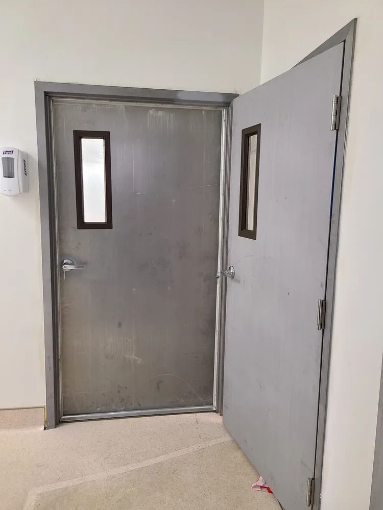 Gray metal doors in a hallway, one open with narrow windows.