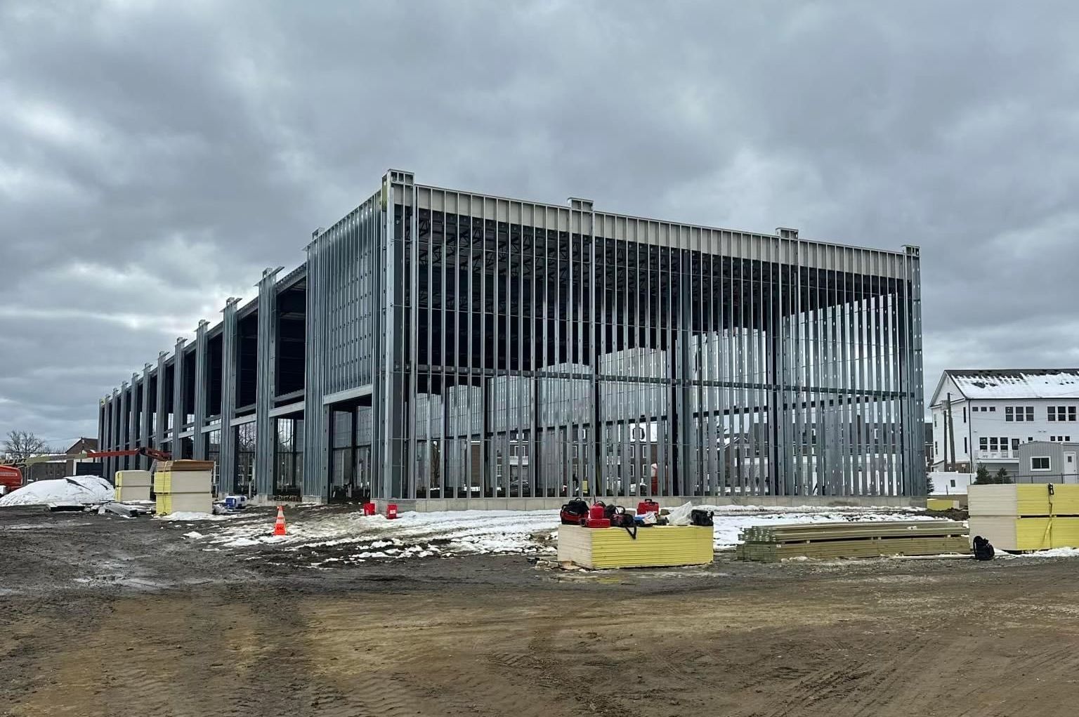 A large building under construction in a field with a cloudy sky in the background.