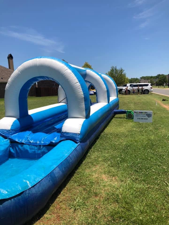 Blue inflatable water slide with white arches on a grassy lawn near a house and parked vehicles