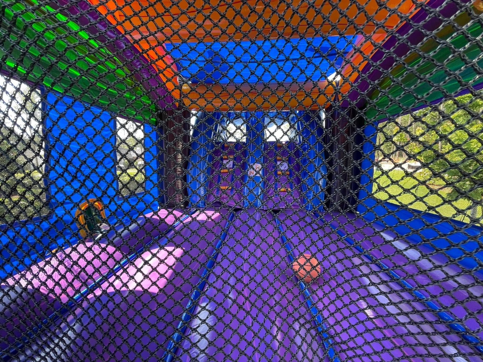 Colorful indoor bouncy play area with netted walls, blue and purple floors, and a child playing inside