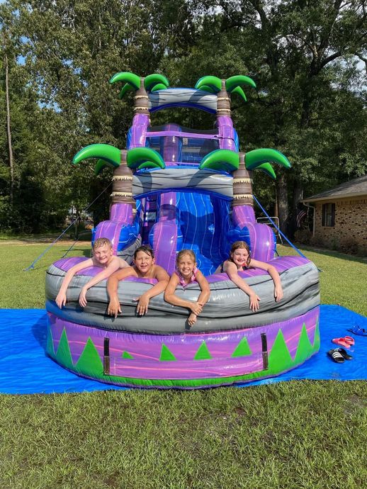 Four kids in swimsuits on a colorful tropical bounce house in a grassy yard