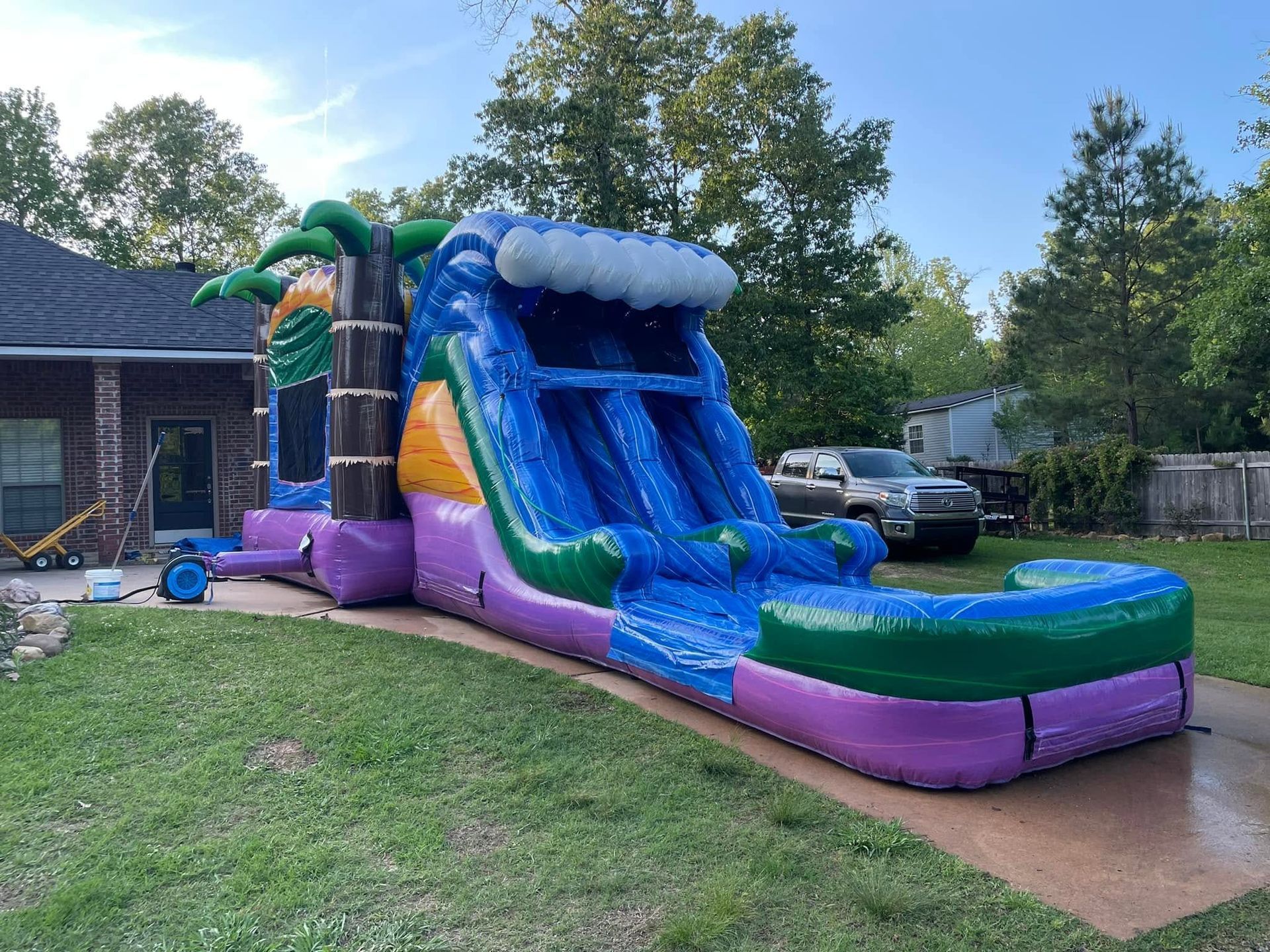 Colorful inflatable water slide in a backyard, with blue chute and purple base beside a wet patio.