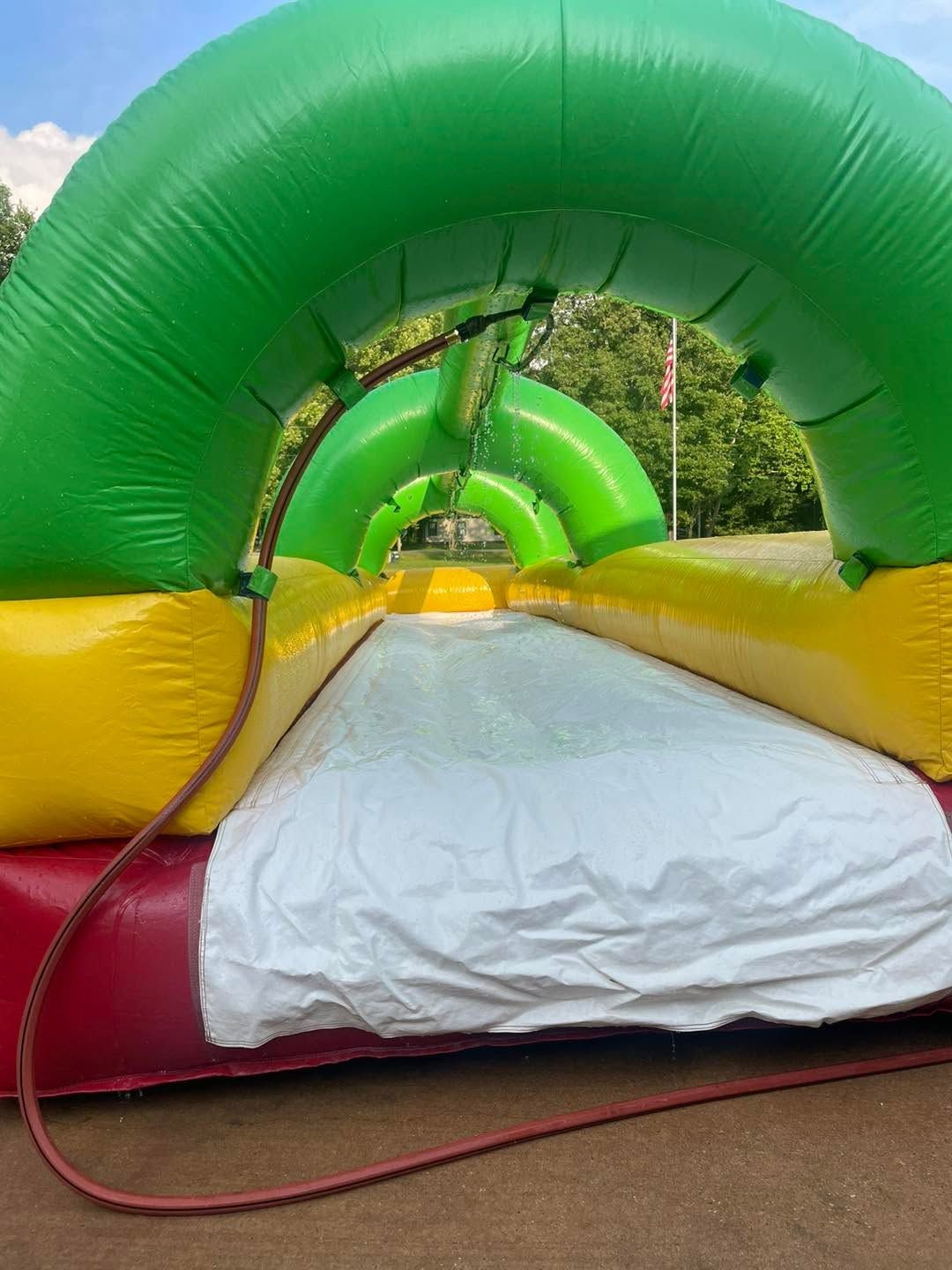 Colorful inflatable obstacle tunnel in green, yellow, and red with a white landing mat outdoors.