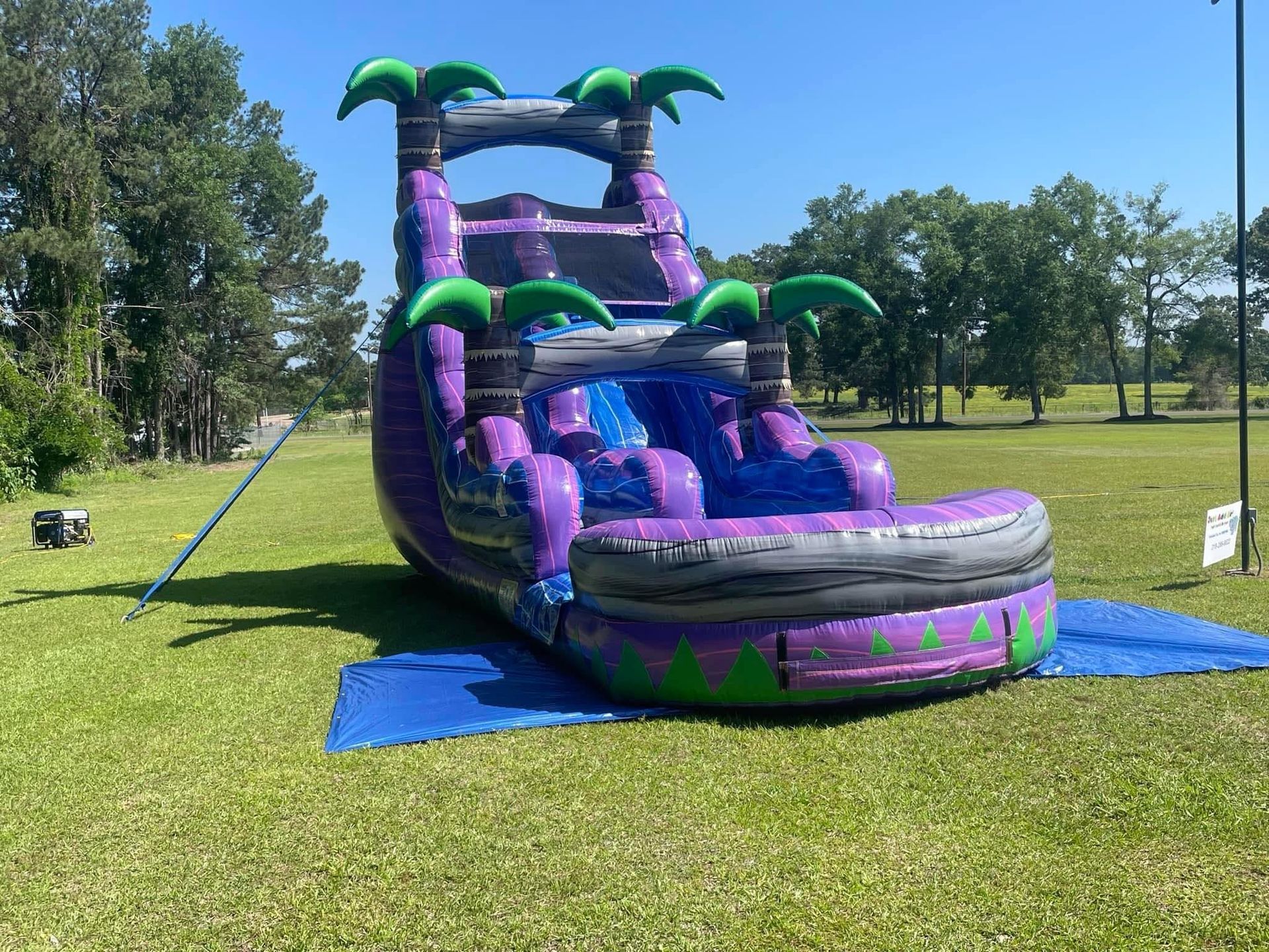 Purple-and-green inflatable water slide on a grassy field under a sunny sky