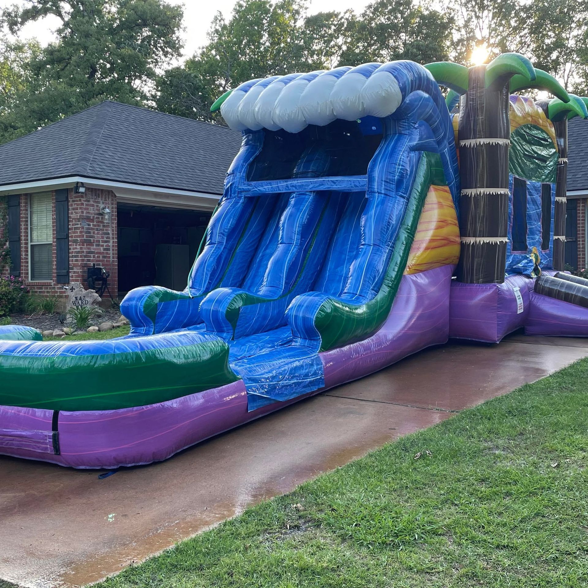 Blue inflatable water slide beside a brick house, with water flowing down the front.