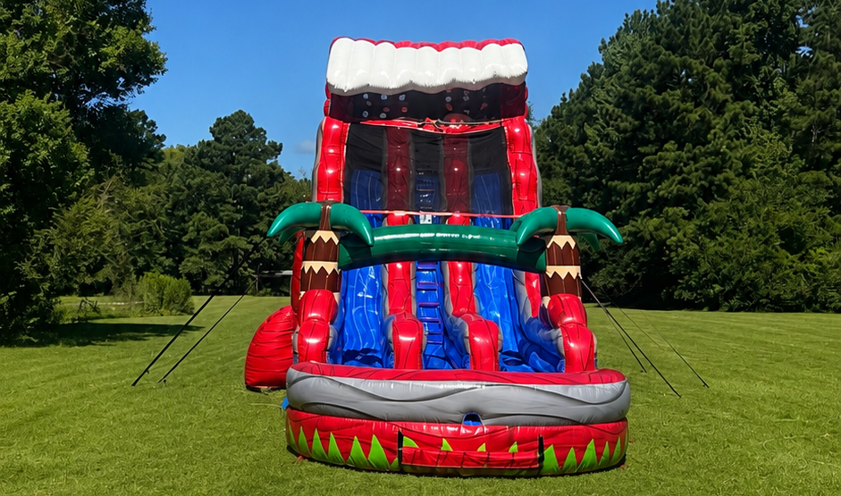 Red, white, and blue inflatable water slide on a grassy field with trees in the background