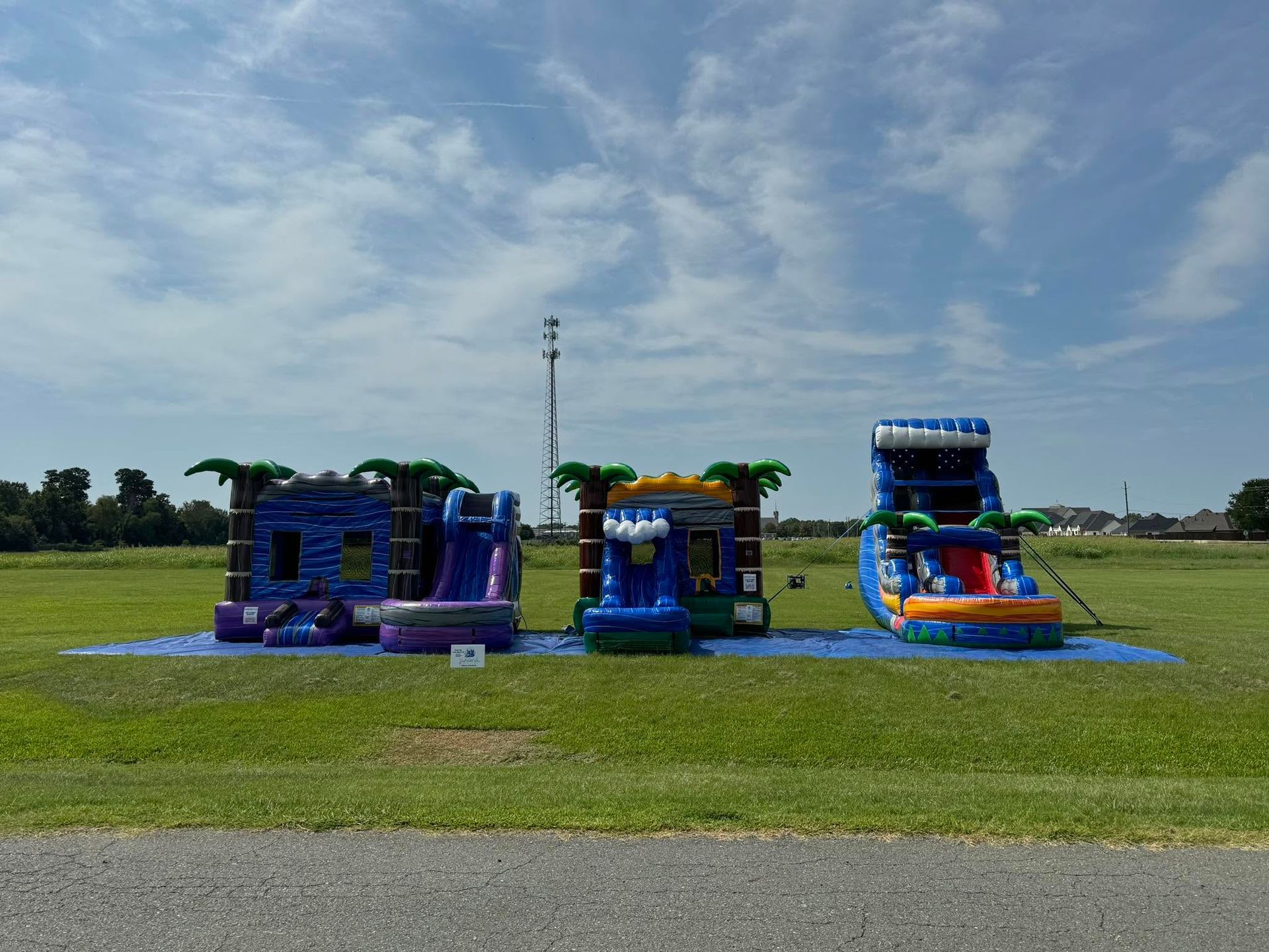 Three blue and orange bounce houses on a grassy field under a partly cloudy sky.