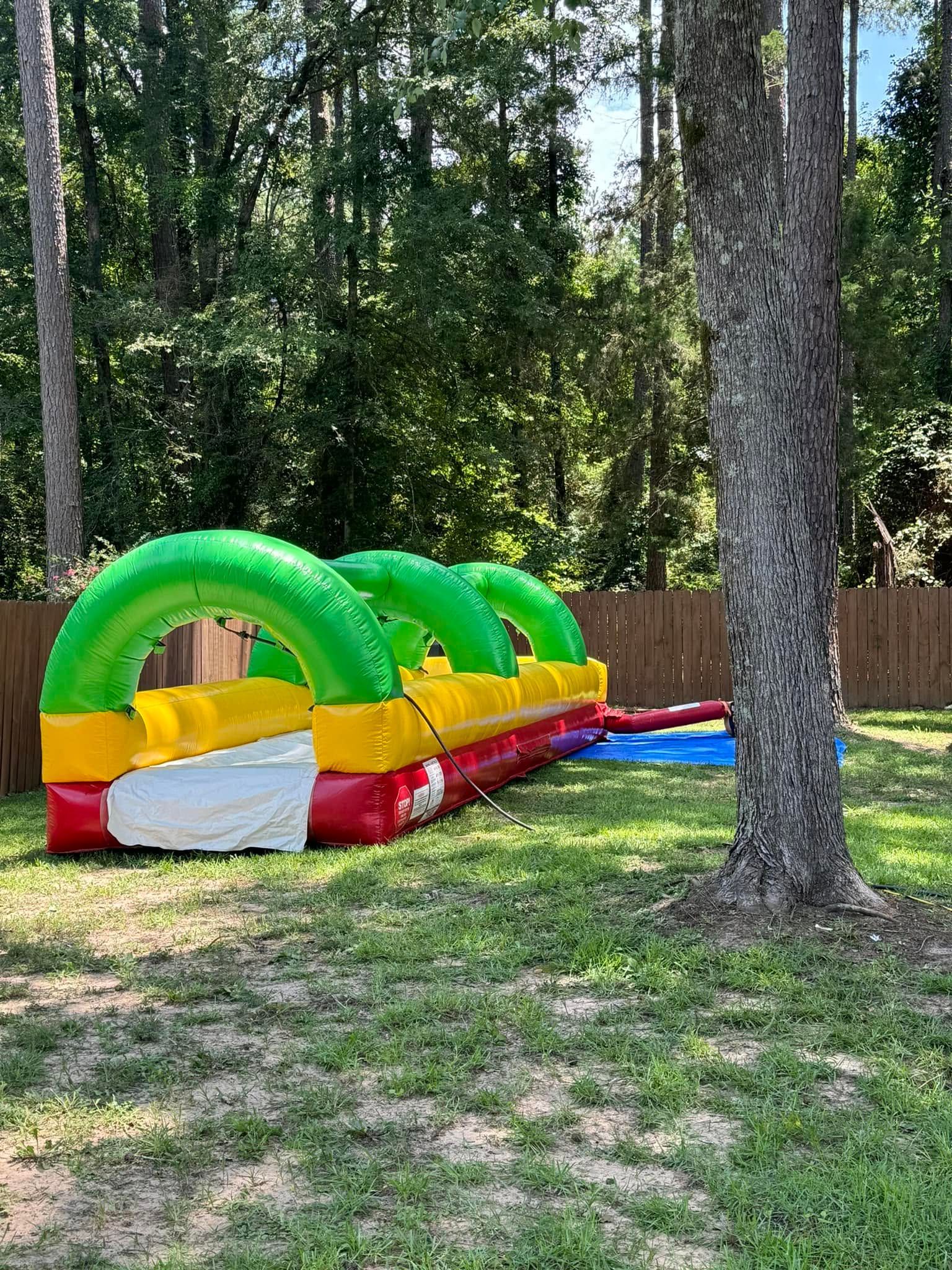 Inflatable green-and-yellow obstacle course in a wooded park on grass