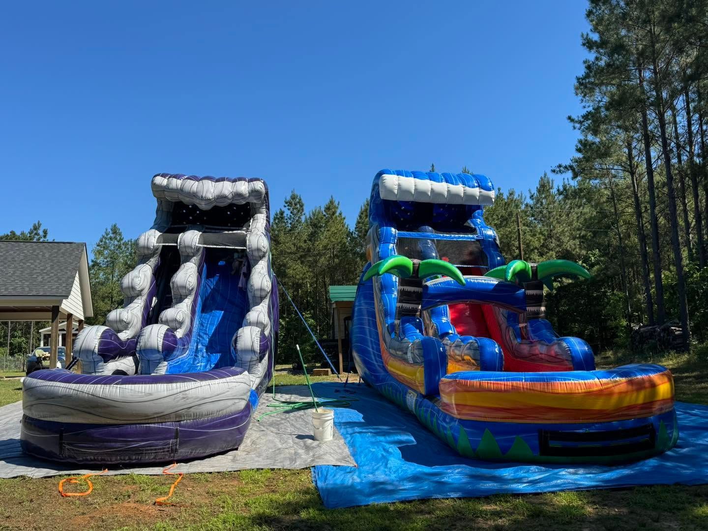 Two inflatable water slides, gray and blue, on a sunny backyard lawn under a clear sky