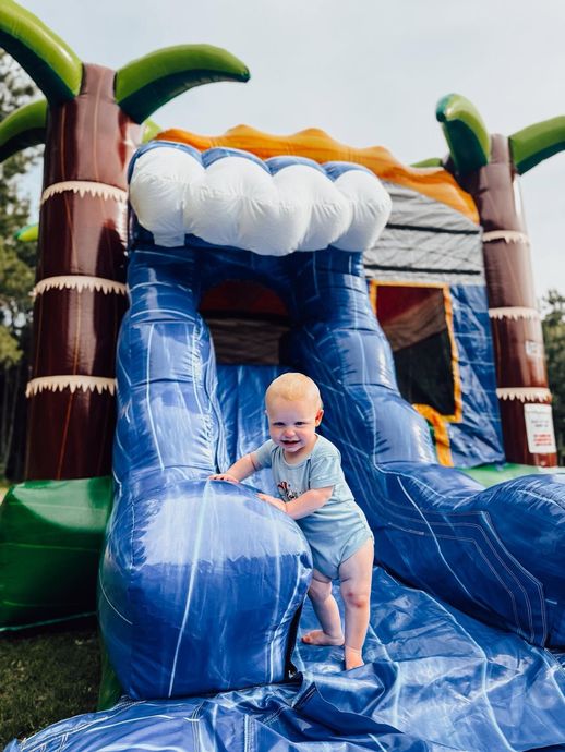 Child sliding down a blue inflatable water slide at a bounce house