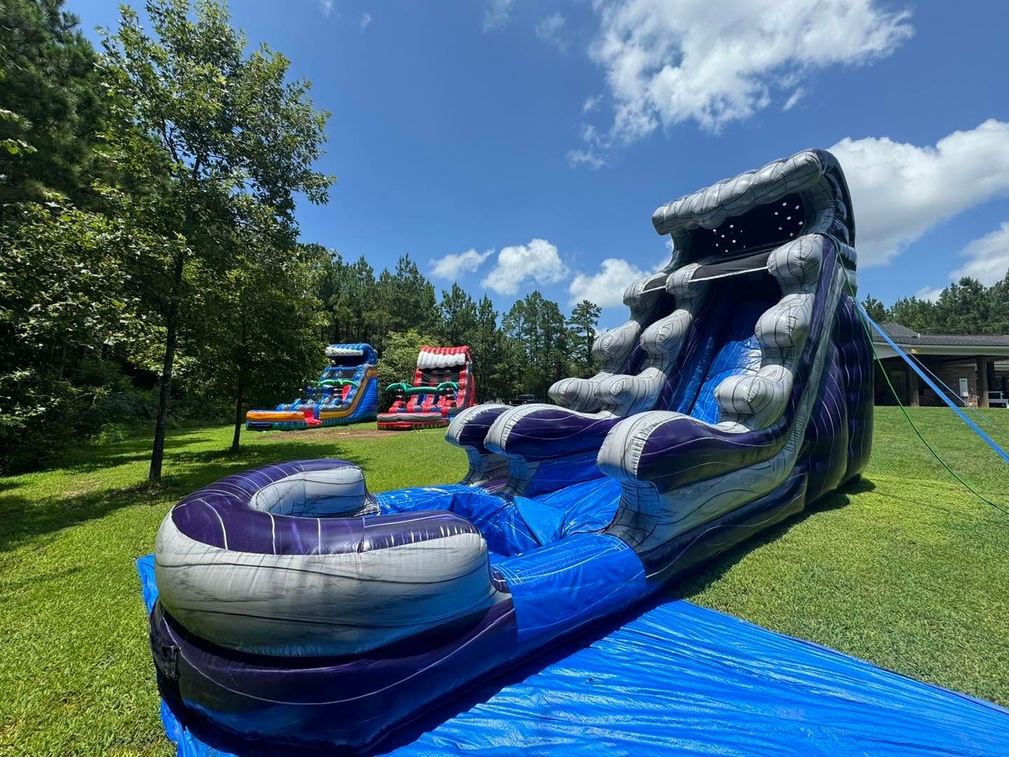 Blue inflatable water slide with a splash pool on a grassy field under a sunny sky
